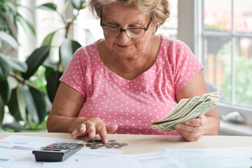 Senior woman sitting at desk counting money to pay bills