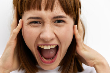 a close horizontal studio photo of a red-haired woman screaming loudly clutching her head from shock.