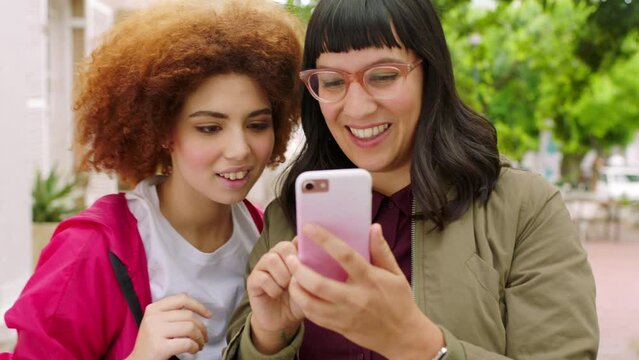 Playful female friends taking selfies with a phone outside in an urban park. Happy girls posing for a photograph to post on social media. Young women smiling and laughing together making memories