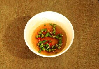 Brown fish sauce with fresh cut chilli in white cup on wood background, Thai style