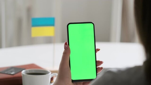Use green screen for copy space closeup. Chroma key mock-up on smartphone in hand. Woman holds mobile phone. On the table is the flag of Ukraine.
