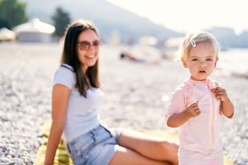 Fototapeta na wymiar Little girl stands on the beach near smiling mom