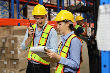Group of warehouse workers with hardhats and reflective jackets using tablet, walkie talkie radio and cardboard while controlling stock and inventory in retail warehouse logistics, distribution center