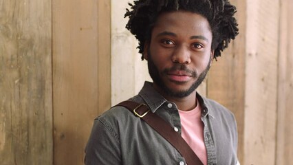 Portrait of a happy black man using a phone against a wooden background with copyspace. Smiling African American man texting and checking social media while waiting for a cab on his daily commute