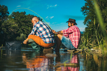 Two men friends fisherman fishing on river. Old father and son with rod fishing at riverside. Recreational activity.