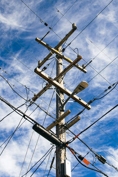 A utility pole (telephone pole) is crowded with cable, telephone, telecom and electrical wires against a blue sky background.