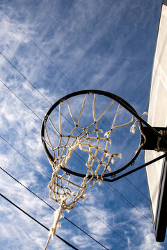 A ragged basketball net hangs from a backboard against a blue sky background.