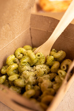 Pesto pasta is served in a compostable container with a compostable wooden fork.
