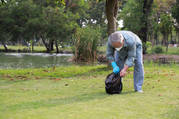 Naklejka na ściany i meble volunteer tourist asian senior man cleaning up garbage and plastic debris on dirty park by collecting them into big black bag