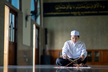 A little Asian Muslim boy is sitting and reading the Quran. The peace in the mosque makes it an energetic atmosphere of faith, with copy space.