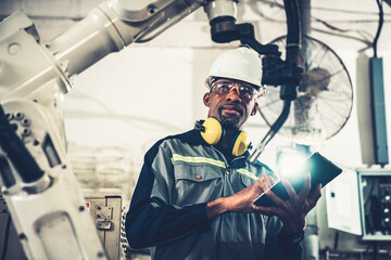 African American factory worker working with adept robotic arm in a workshop . Industry robot...