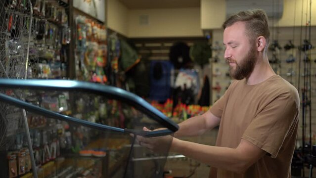 a man fisherman in a fish tackle shop chooses a landing net for fishing.