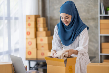 Muslim young Asian woman working at home doing sme ecommerce online small business entrepreneur checking postal parcels to delivery to online customers, startup Muslim Sme business concept.