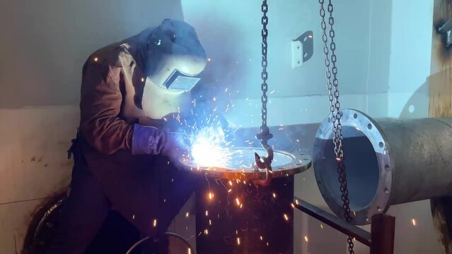 Repair of a marine vessel, a welder in protective glasses does welding of a larger pipe, a technological process.
