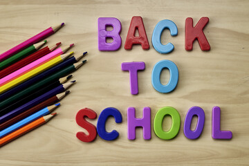 the phrase back to school is laid out in multicolored letters on the table next to colored pencils the concept of education school