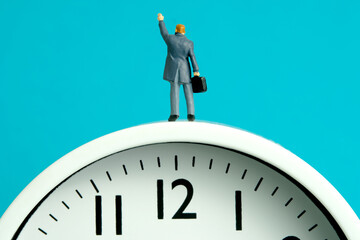 Miniature people toy figure photography. Time management power concept. A businessman standing above clock while raise his hand. Isolated on blue background