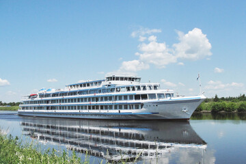 A white ship sails along the river on a clear summer day. 