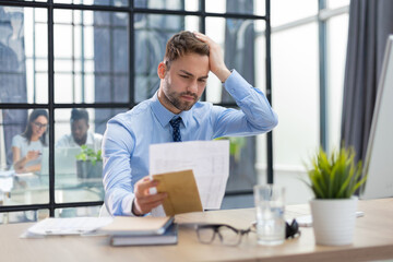 Handsome entrepreneur reading a letter from envelope in a desktop at office with collegues on the...