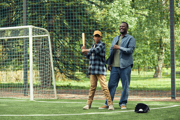 African happy dad learning his son to play baseball on the field outdoors