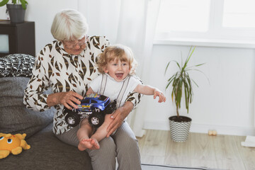 Elderly woman with her little grandson playing at home on the sofa