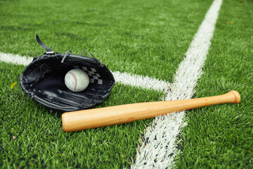 Close-up of baseball glove with ball and bat on green field preparing for baseball game