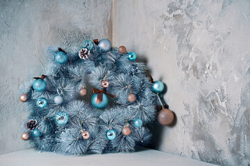 Traditional Christmas decorative wreath over grey marble wall. Holiday interior details. Round fir garland with snow, blue glitter balls and pine cones. Copy space for New Year congratulations.