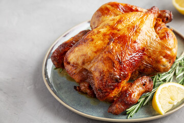 Homemade Lemon and Herb Rotisserie Chicken on a Plate on a gray background, side view.