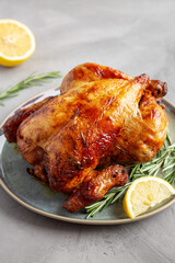 Homemade Lemon and Herb Rotisserie Chicken on a Plate on a gray surface, side view.