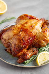 Homemade Lemon and Herb Rotisserie Chicken on a Plate on a gray background, side view. Close-up.