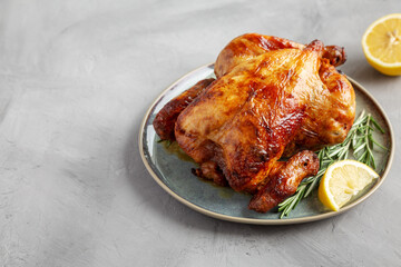 Homemade Lemon and Herb Rotisserie Chicken on a Plate on a gray surface, side view. Copy space.