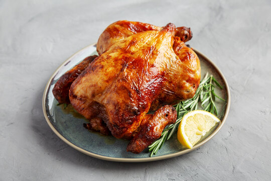 Homemade Lemon and Herb Rotisserie Chicken on a Plateon a gray background, side view.