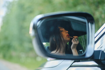 Naklejka premium Reflection in rear view mirror of a woman applying lipstick while sitting in the car
