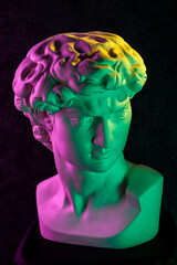 Gypsum copy of head statue David in bright neon colors for artists on a dark background. Face famous sculpture youth of David by Michelangelo. Template design for dj, fashion, poster, zine, collage.