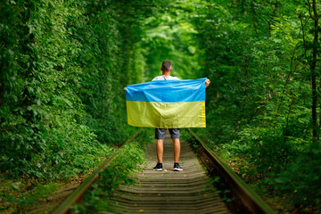 man raised his hands and holds the Ukrainian flag behind his back. concept Ukrainian patriot, rally in support of Ukraine