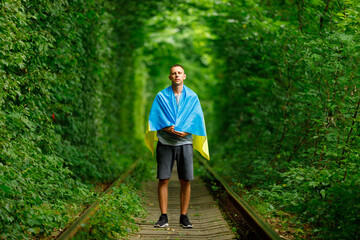 man raised his hands and holds the Ukrainian flag behind his back. concept Ukrainian patriot, rally in support of Ukraine