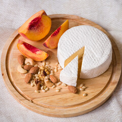 Delicious young homemade Camembert Cheese on a wooden board with peach nuts and slices. Selective focus on a piece of cheese
