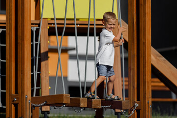Obraz na płótnie Canvas Boy in a white T-shirt and shorts on the playground climbs the climbing wall. games on the street