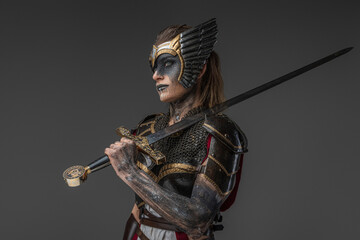 Shot of strong warrior woman from past holding sword on her shoulder against gray background.