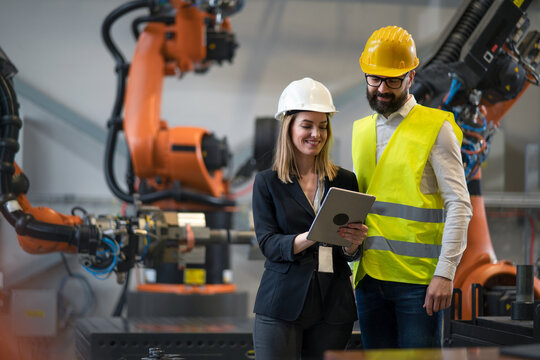 Chief engineer and project manager in modern industrial factory with robot arms talking and planning optimization of production.