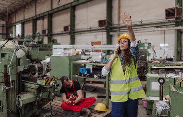 Woman is calling ambulance for her colleague after accident in factory. First aid support on...
