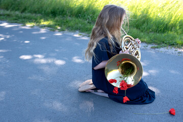 Teen girl playing french horn outdoors. Decorated with red poppies.