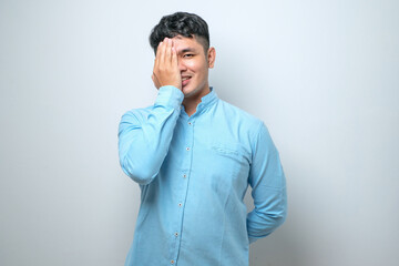 Young handsome asian man covering one eye with hand, confident smile on face and surprise emotion.