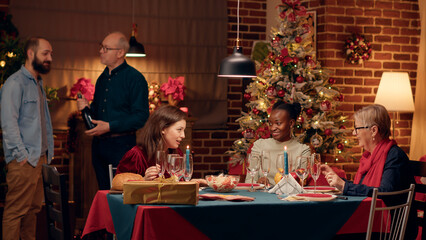 Festive diverse people at home enjoying Christmas dinner together. Joyful multiracial family members celebrating winter feast with salad and traditiona home cooked food while talking.