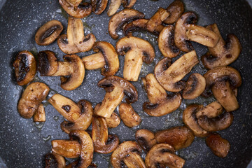 Sliced mushrooms in a frying pan on induction hob at domestic kitchen