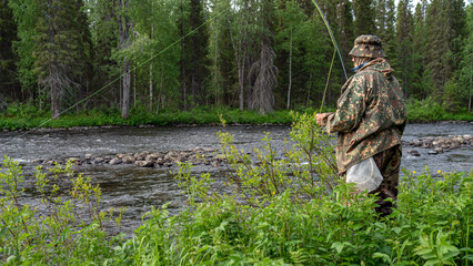 A fisherman in a mountain river catches trout, morning. Side view.