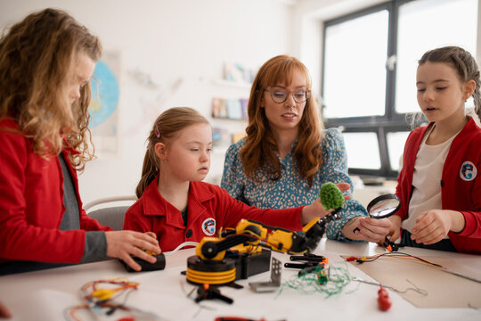Group of kids with young science teacher programming electric toys and robots at robotics classroom