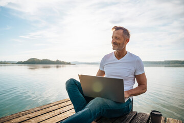 Happy freelancer with laptop and enjoying view from pier