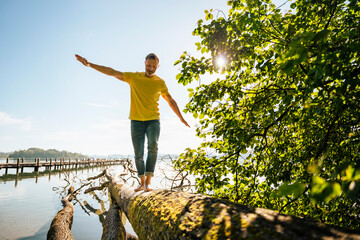 Mature man balancing on fallen tree at lakeshore