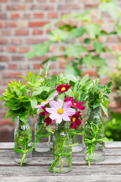 Fresh herbs and flowers in decorated glass bottles standing on balcony table