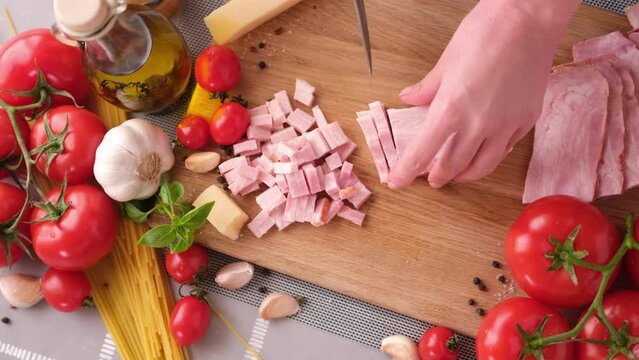Making pasta carbonara - Slicing traditional pancetta bacon into pieces on a wooden cutting board with a knife